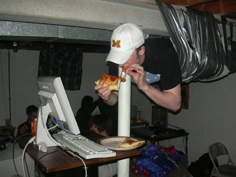 A gamer duct-taped to the ceiling of a room during a LAN party